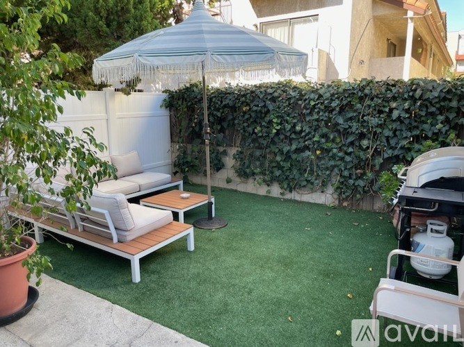 A patio with a white umbrella and a white couch.