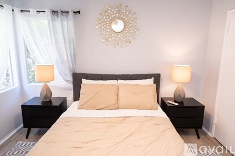 A bedroom with a large bed, two nightstands with lamps, and a decorative wall mirror.