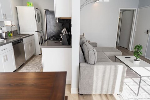 A modern kitchen with a dining table and a grey couch in the living room.