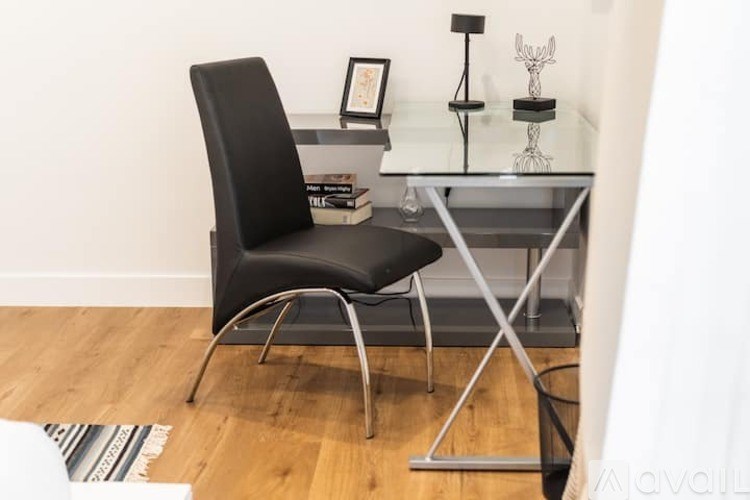 A black chair sits in front of a glass table with a metal frame.