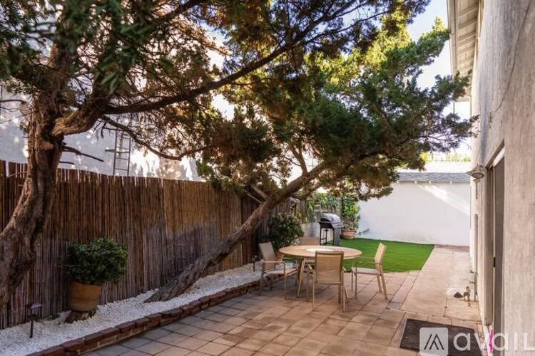 A patio with a table and chairs is surrounded by a wooden fence and a tree.