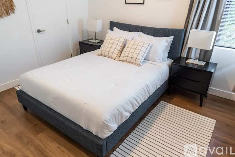 A bed with a white comforter and two pillows sits on a wooden floor in a room.