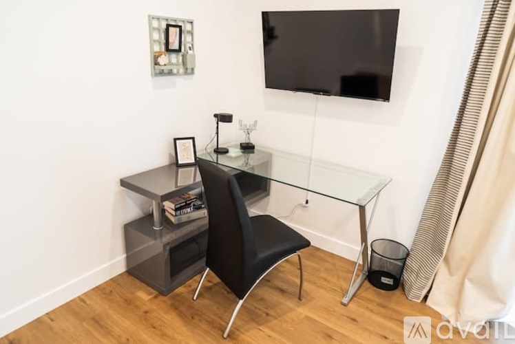 A black chair is placed in front of a glass desk with a black box and a black trash bin.