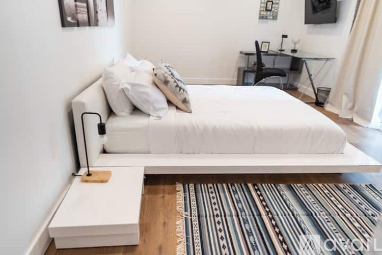 A white bed with a wooden headboard and footboard sits in a room with a striped rug in front of it.