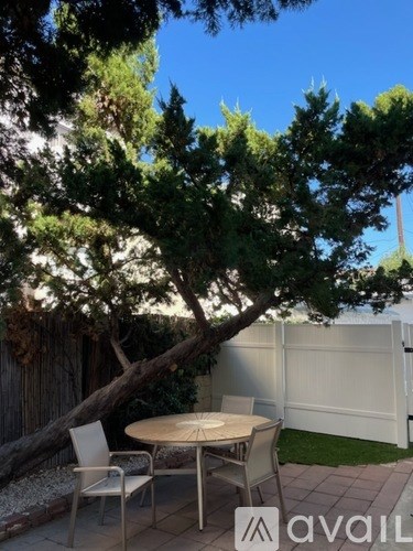 A patio with a table and chairs is surrounded by a white fence and trees.