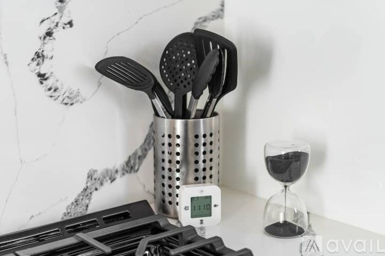 A kitchen counter with utensils, a timer, and a glass of wine.