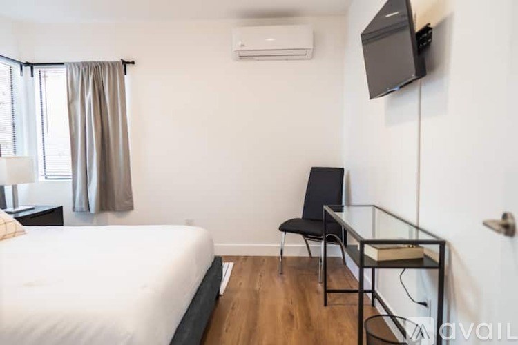 A bedroom with a bed, chair, and a television mounted on the wall.