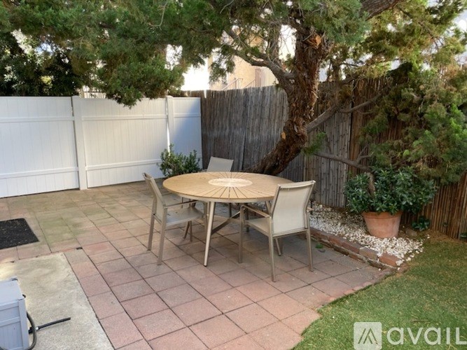 A patio with a table and chairs surrounded by a fence and a tree.