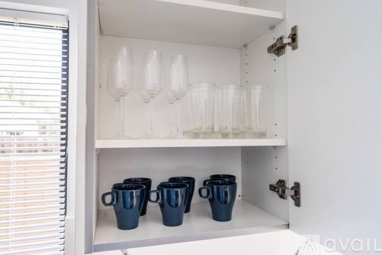 A white cabinet with three blue cups and three clear glasses on top.
