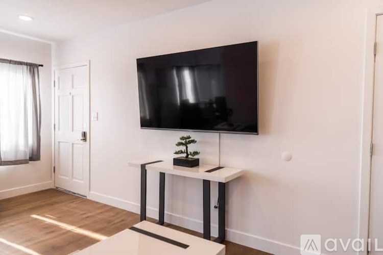 A black television is mounted on a white wall above a white console table with a plant on it.