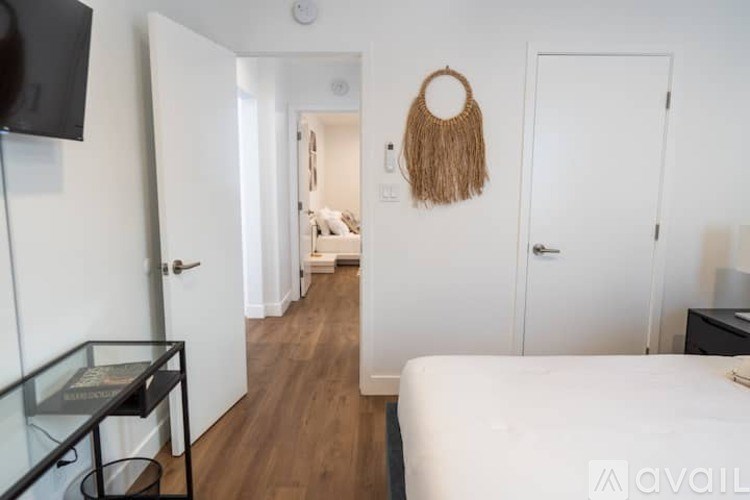 A bedroom with a bed, a glass table, and a woven bag hanging on the wall.