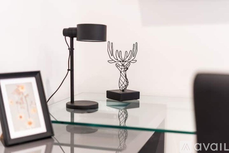 A glass table with a lamp, a picture frame, and a sculpture on it.