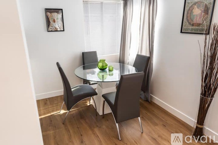 A glass dining table with four chairs and a vase with green plants on it.