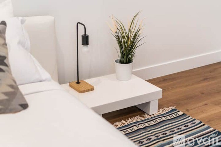 A white bedside table with a plant and a lamp on it.