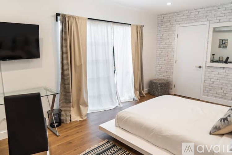 A bedroom with a large bed, a flat screen TV, and a white brick wall.