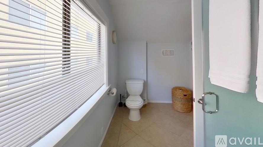 A bathroom with a toilet, a window with blinds, and a basket on the floor.