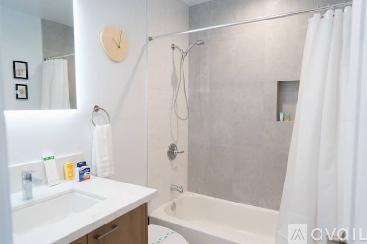 A bathroom with a white sink, a shower with a white curtain, and a clock on the wall.