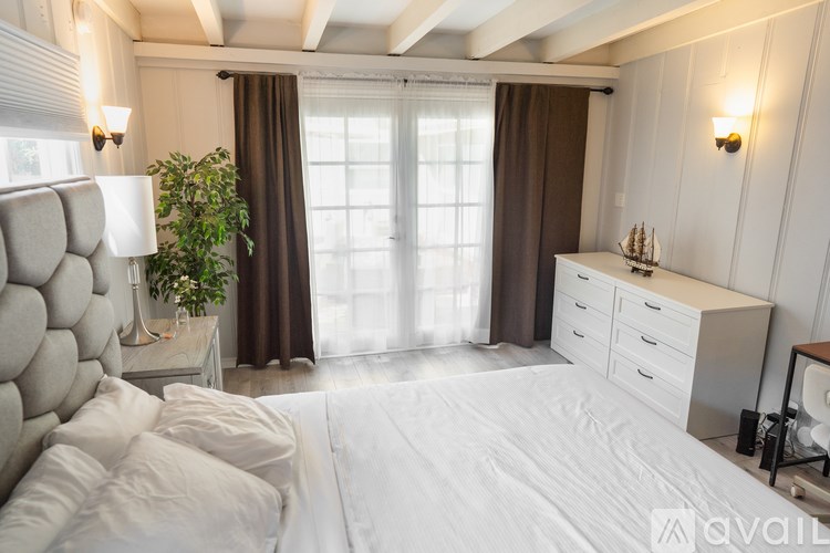 A bedroom with a large bed, a nightstand, and a window with curtains.