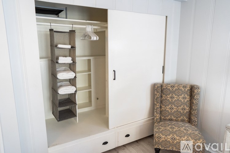 A chair is placed in front of a white cabinet with a shelf and towels.