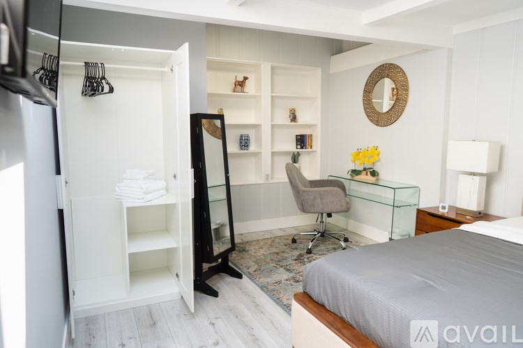 A bedroom with a bed, desk, chair, and a mirror on the wall.