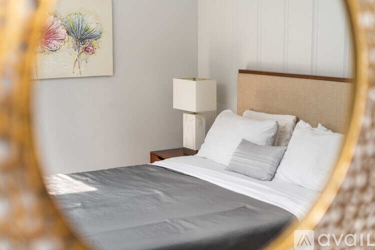 A bed with white pillows and a grey bedspread is reflected in a mirror.