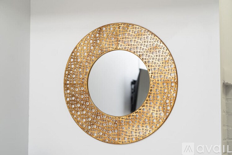 A round mirror with a gold frame is hanging on a white wall.