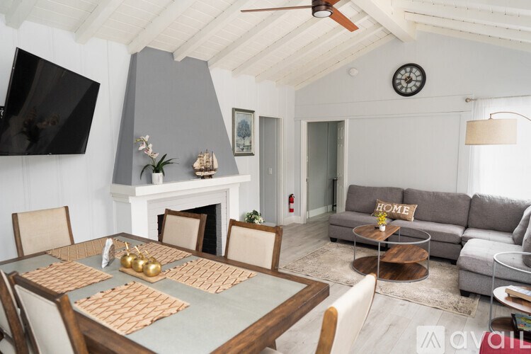 A living room with a grey couch, a wooden dining table and a television on the wall.
