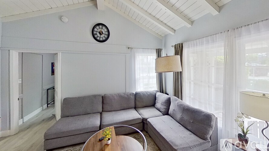 A grey couch sits in a living room with a clock on the wall.