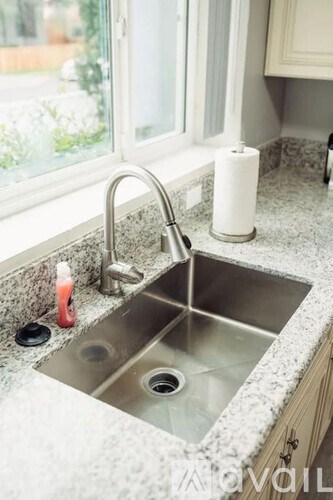 A kitchen sink with a silver faucet and a red bottle of dish soap on the countertop.
