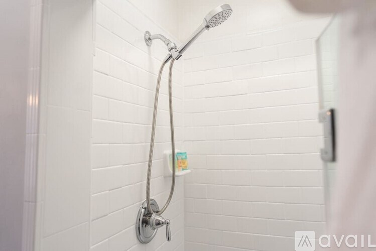 A white tiled shower with a handheld shower head and a hose.