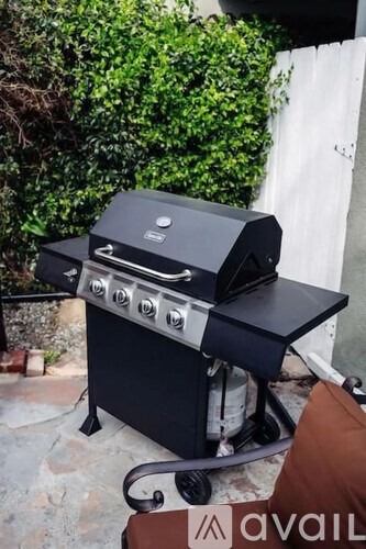 A black outdoor grill with four burners and a side shelf is placed on a patio.