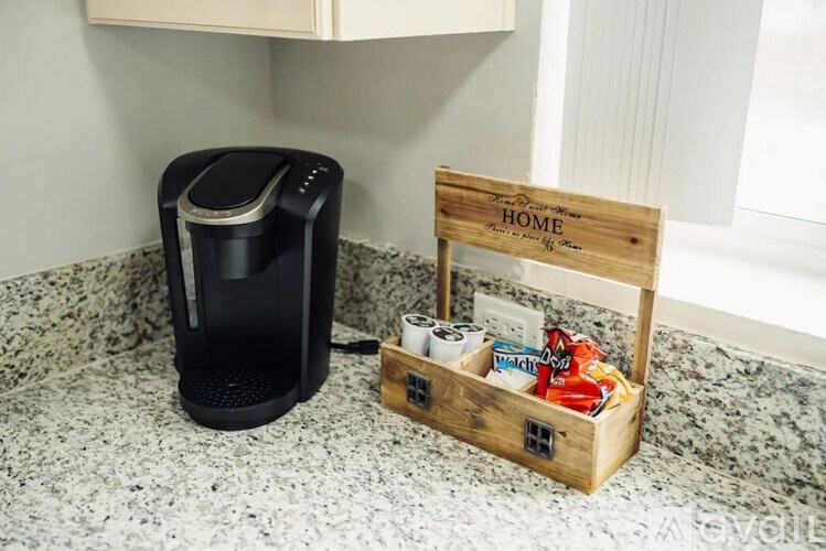 A black coffee maker and a wooden crate with snacks on a granite countertop.