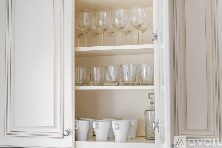 A white cabinet is open, revealing a shelf with glasses and cups.