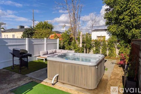A hot tub is in the middle of a backyard with a patio and a grill.
