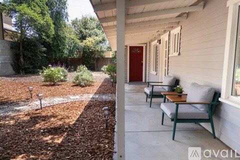 A patio with a table and chairs is surrounded by a gravel area and trees.