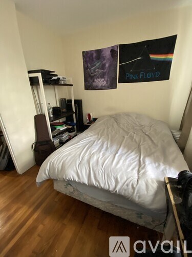 A bedroom with a bed, a poster of Pink Floyd, and a wooden floor.