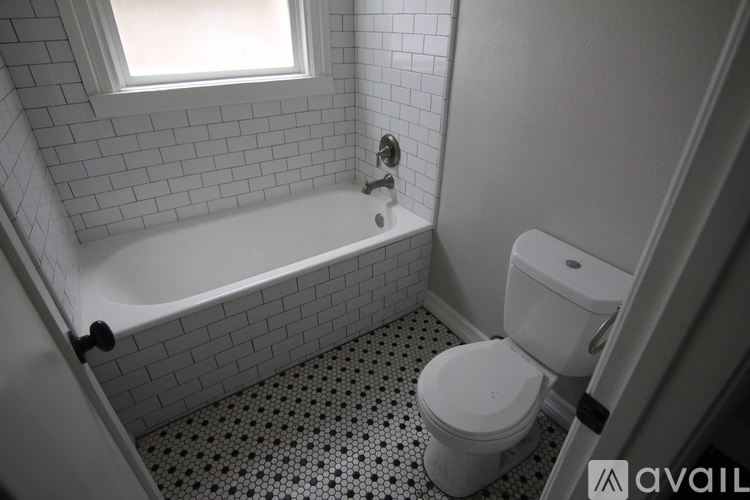 A white toilet sits next to a bathtub in a bathroom with black and white tile flooring.