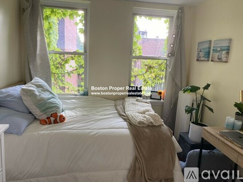 A bedroom with a bed, a window with curtains, a nightstand with a lamp, a plant, and a picture on the wall.