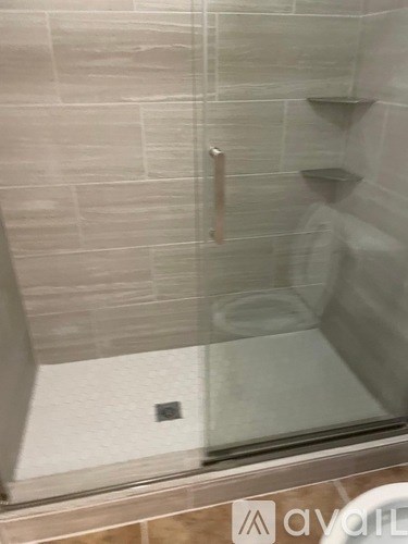 A shower with a glass door and a metallic handle.