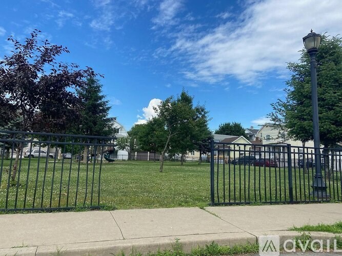 A black metal fence surrounds a grassy area with trees and a street lamp.