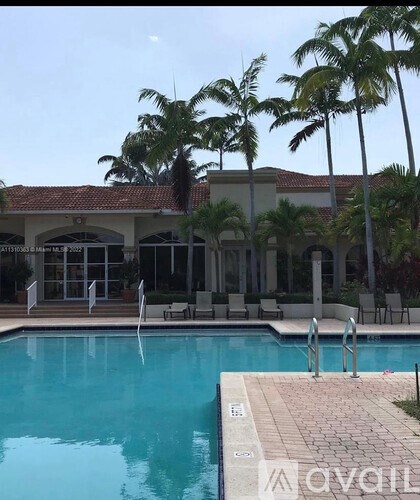 A pool with a building behind it and palm trees in front.