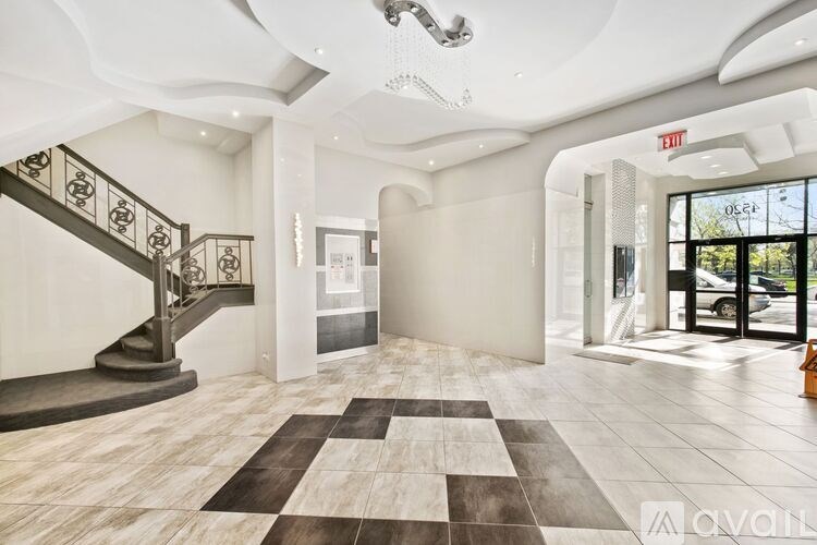 A large, open living space with a checkered rug on the floor and a staircase with a metal railing on the left.