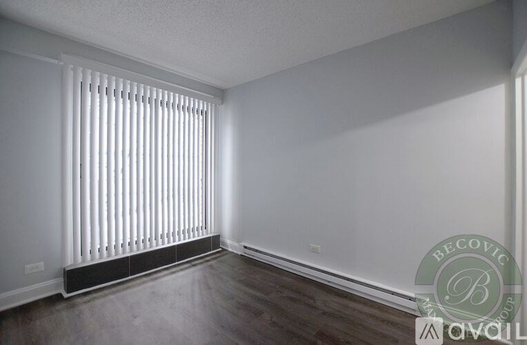 A room with a window covered by white blinds and a wooden floor.