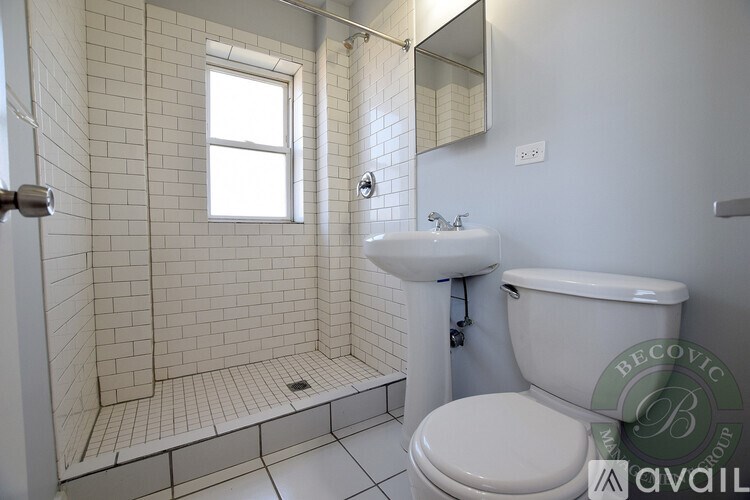 A white bathroom with a toilet, sink, and tiled shower.