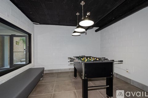 A pool table is in the middle of a room with a bench and a window.