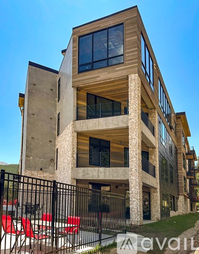 A modern house with a black fence and red chairs in front.