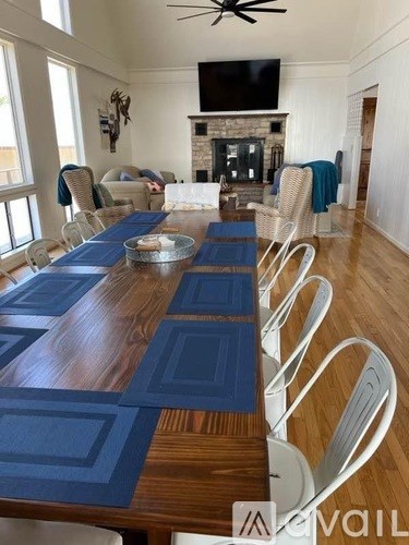 A long wooden table with blue placemats and white chairs in a room with a fireplace.