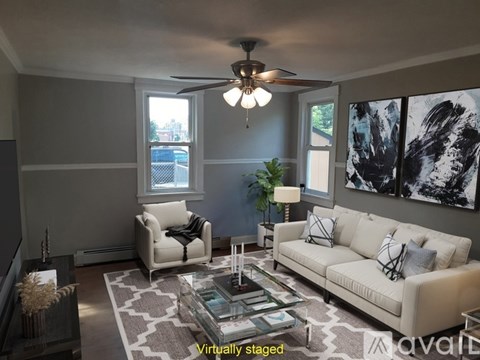 A living room with a white couch, a glass coffee table, and a ceiling fan.