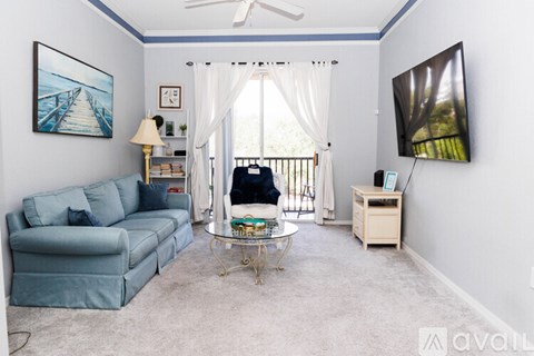 A living room with a blue couch, a fan, a television, and a painting on the wall.