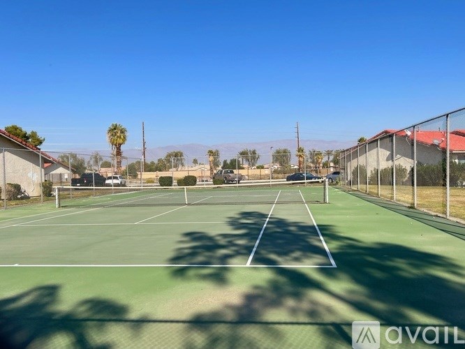 A tennis court with a clear blue sky and shadows of trees on the ground.